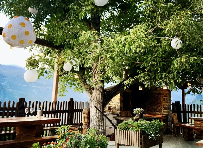 Terrasse ombragée avec lampions, tables en bois et vue sur la vallée
